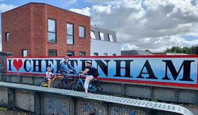 Cyclists in front of a Cheltenham sign