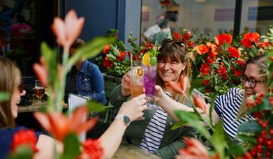 A group of women raising a toast with colourful cocktails in Flight Club's flowery summer terrace