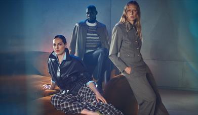 3 adults modelling new Autumn Winter clothes sat on a sofa.